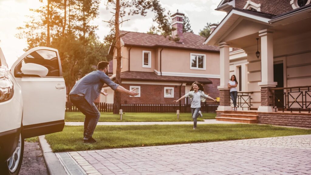 happy family. dad came home, daughter is running out to meet him while wife is waiting on the house's porch.