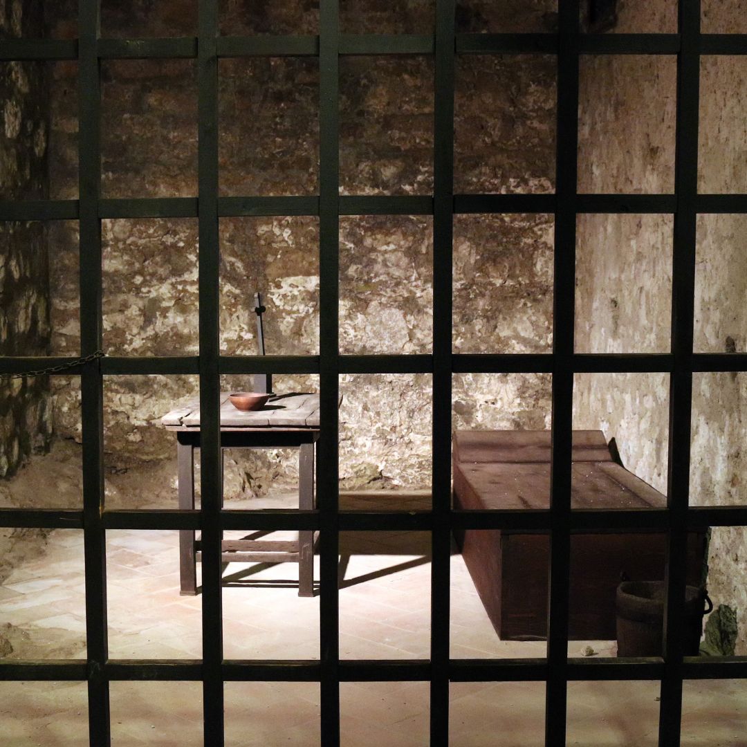 image of an old prison cell, with a bed and a table with a cup on it