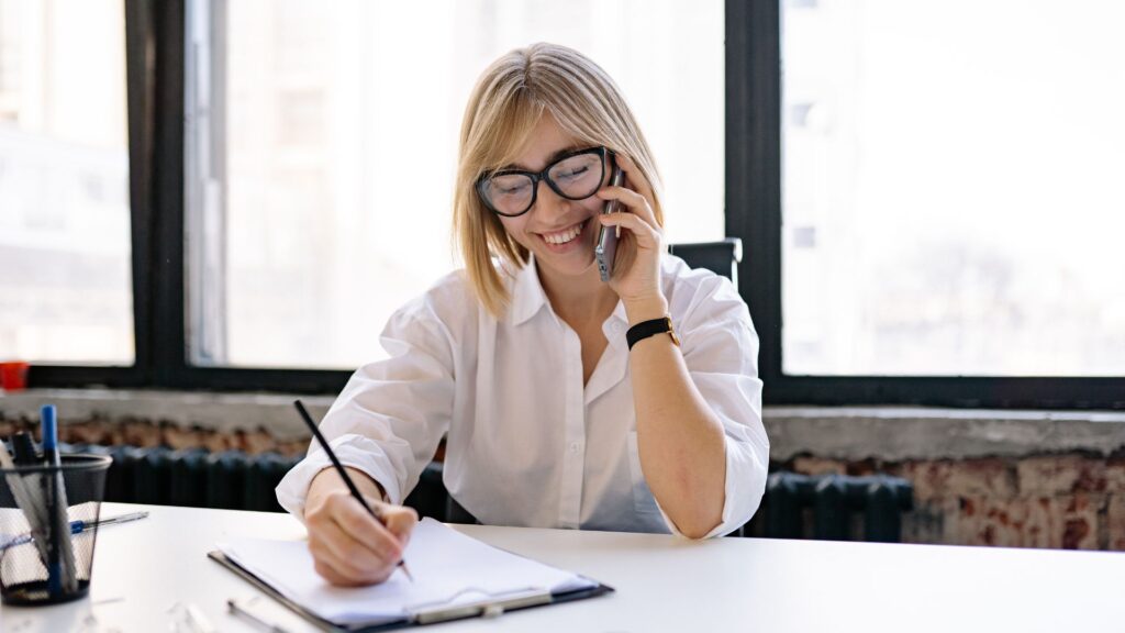professional woman sits at desk and hold phone and pen in the other hand