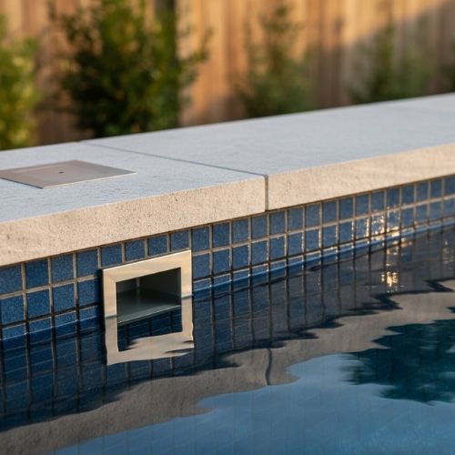 Close-up detail of the stone coping and blue tile of a modern plunge swimming pool.