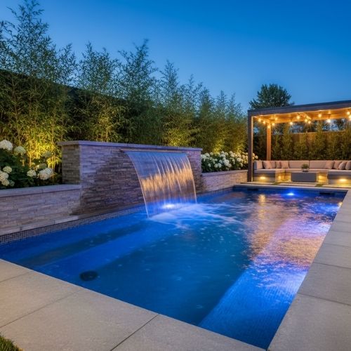 A swim spa plunge pool with a cascading water feature and ambient lighting at dusk.